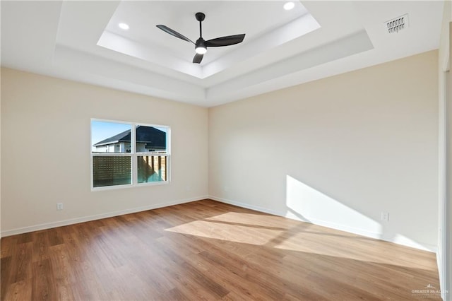 spare room featuring a ceiling fan, a tray ceiling, visible vents, and wood finished floors