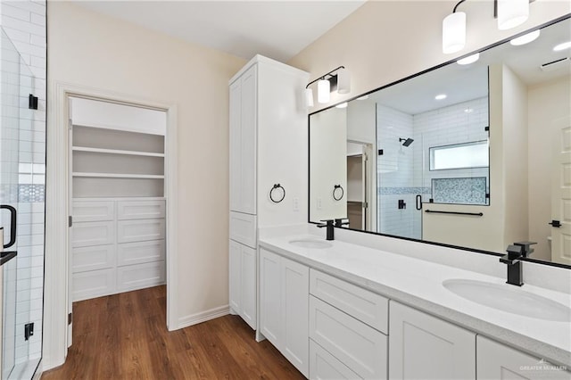 full bath featuring double vanity, a stall shower, a sink, and wood finished floors