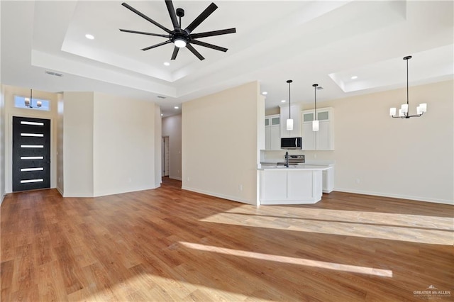 unfurnished living room with light wood finished floors, a raised ceiling, visible vents, baseboards, and ceiling fan with notable chandelier