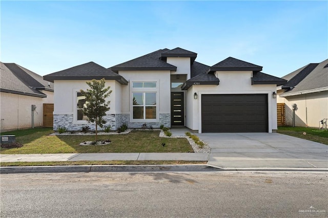 prairie-style house featuring stucco siding, an attached garage, a front yard, stone siding, and driveway