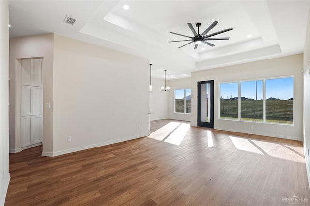 empty room with ceiling fan with notable chandelier, wood finished floors, visible vents, baseboards, and a tray ceiling