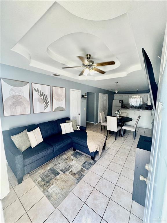 living area with light tile patterned floors, a ceiling fan, visible vents, and a raised ceiling
