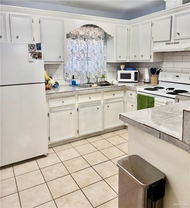 kitchen with white cabinets, under cabinet range hood, light countertops, a sink, and white appliances