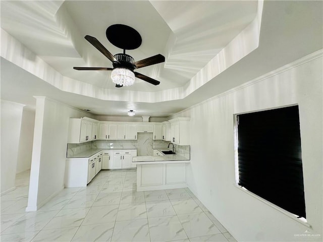 kitchen with sink, backsplash, kitchen peninsula, white cabinets, and a raised ceiling