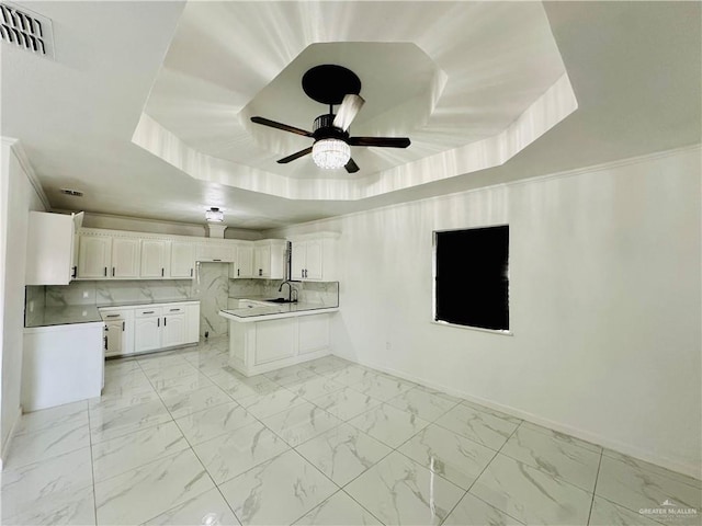 kitchen with tasteful backsplash, white cabinetry, a raised ceiling, and kitchen peninsula