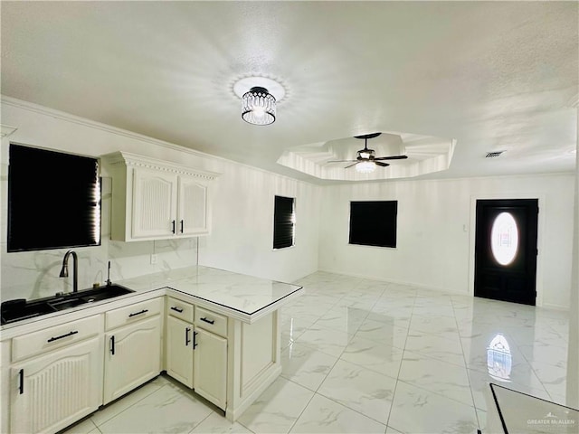 kitchen with ceiling fan, a raised ceiling, sink, white cabinetry, and kitchen peninsula