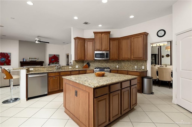 kitchen with stainless steel appliances, a center island, light stone counters, light tile patterned flooring, and kitchen peninsula