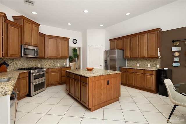 kitchen with stainless steel appliances, light tile patterned flooring, a kitchen island, and light stone countertops