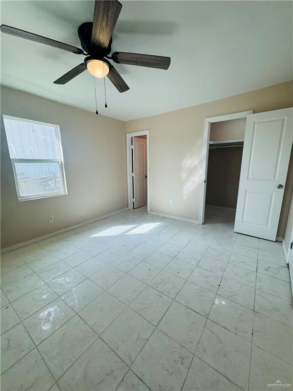 unfurnished bedroom featuring marble finish floor, a spacious closet, baseboards, and a ceiling fan