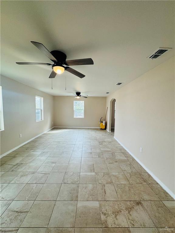 empty room with light tile patterned floors, baseboards, visible vents, and arched walkways