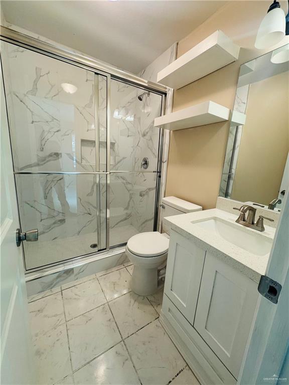 bathroom featuring marble finish floor, toilet, vanity, and a marble finish shower