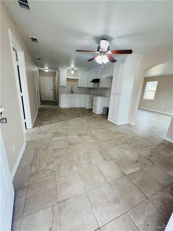 kitchen with arched walkways, under cabinet range hood, visible vents, and white cabinets