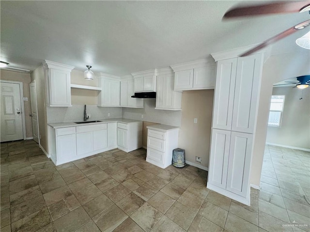 kitchen with baseboards, a ceiling fan, under cabinet range hood, white cabinetry, and a sink