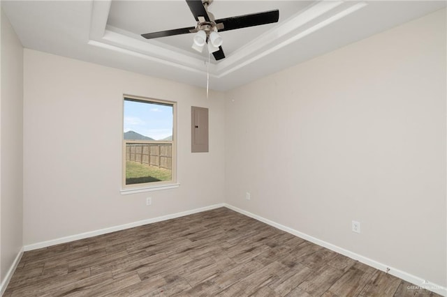 unfurnished room featuring a raised ceiling, electric panel, ceiling fan, and hardwood / wood-style floors