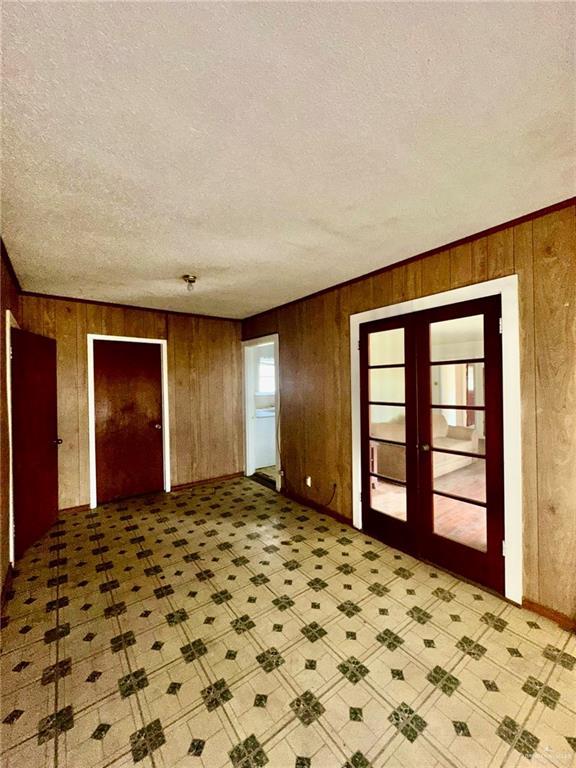 interior space with french doors, a textured ceiling, and wood walls