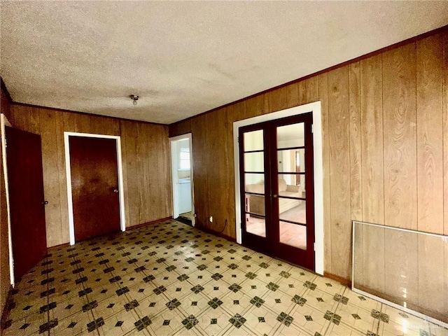 interior space featuring french doors, crown molding, a textured ceiling, and wood walls