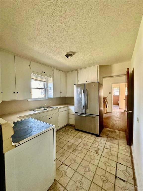 kitchen featuring white cabinetry, sink, stainless steel fridge, stove, and a textured ceiling