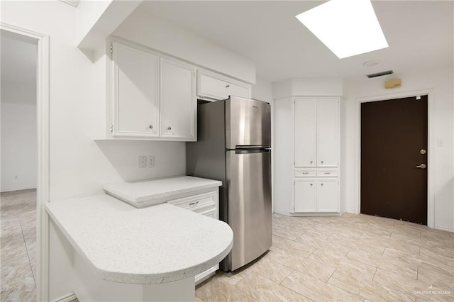 kitchen with white cabinets, kitchen peninsula, stainless steel refrigerator, and a skylight