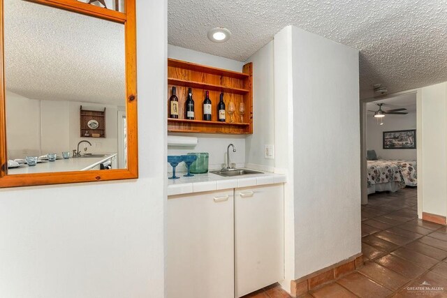 bar with wet bar, a textured ceiling, a ceiling fan, and a sink