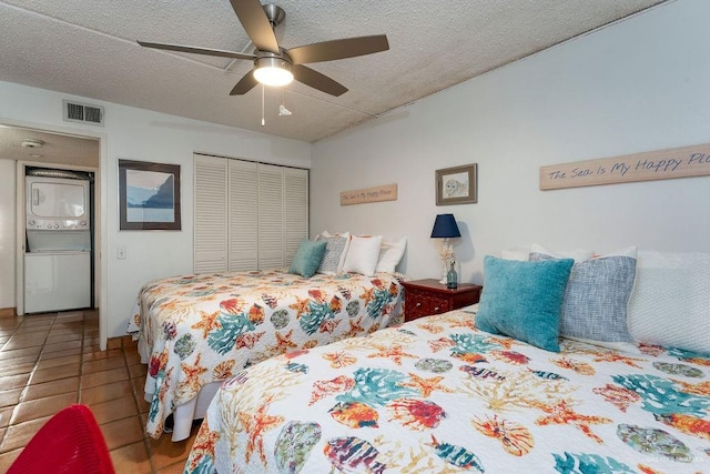 bedroom with visible vents, stacked washer and dryer, a closet, a textured ceiling, and tile patterned floors