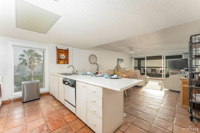 kitchen with a peninsula, white dishwasher, a sink, light countertops, and a textured ceiling