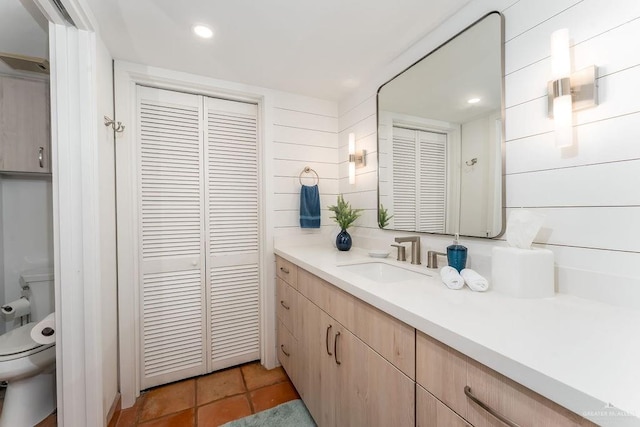 bathroom with a closet, wooden walls, toilet, and vanity