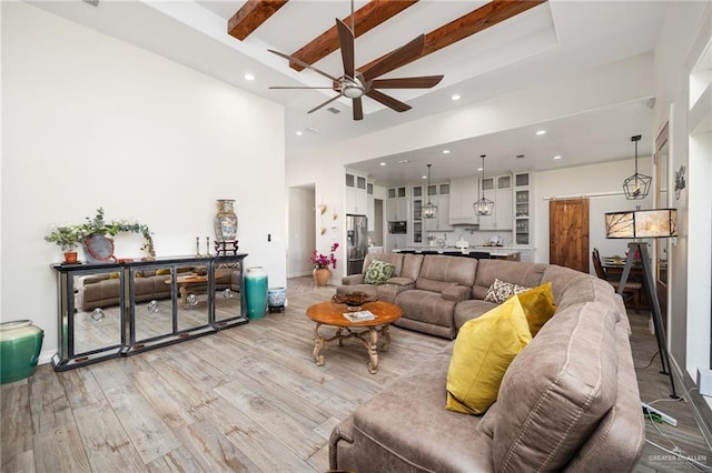 living room featuring beamed ceiling, ceiling fan, a high ceiling, and light hardwood / wood-style flooring