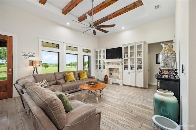 living room featuring beamed ceiling, ceiling fan, a fireplace, and light hardwood / wood-style flooring