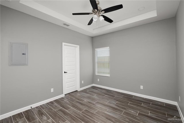 empty room featuring visible vents, electric panel, a tray ceiling, and wood finish floors