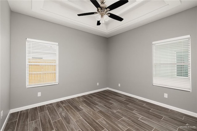 spare room with baseboards, a tray ceiling, ceiling fan, and wood finish floors