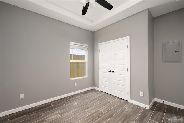 unfurnished bedroom with ceiling fan, baseboards, electric panel, wood tiled floor, and a raised ceiling