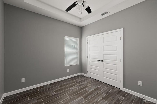 spare room featuring a ceiling fan, baseboards, visible vents, wood tiled floor, and a tray ceiling