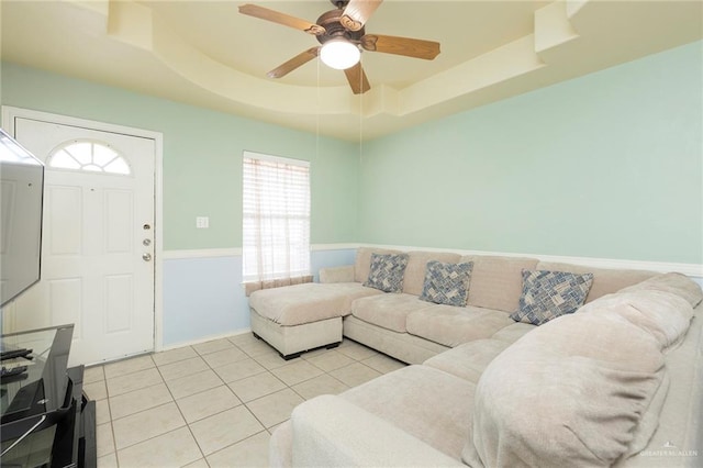 tiled living room with ceiling fan and a tray ceiling