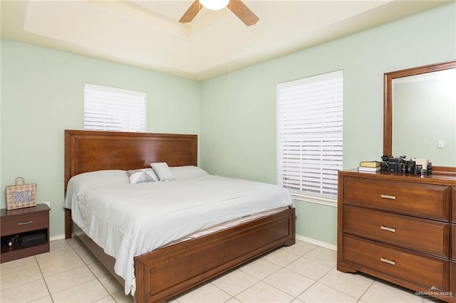 bedroom with ceiling fan, light tile patterned flooring, and a tray ceiling