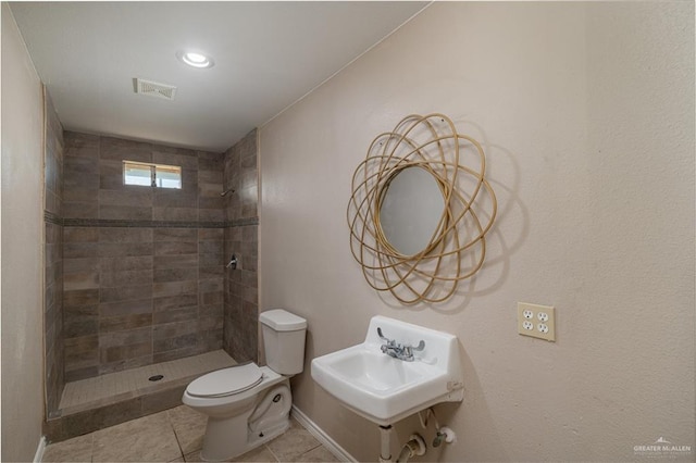 bathroom featuring toilet, tile patterned floors, tiled shower, and sink