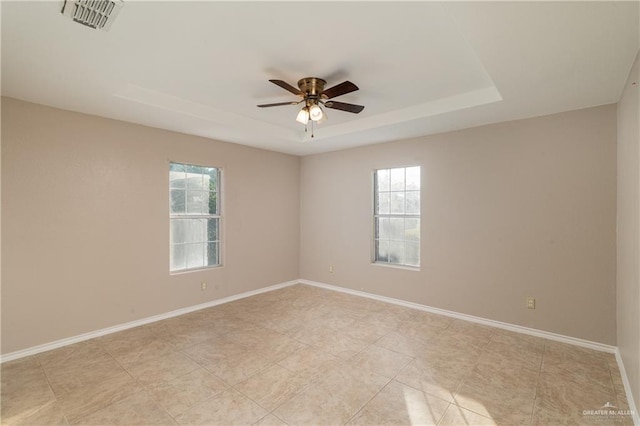 empty room with ceiling fan, plenty of natural light, and a raised ceiling