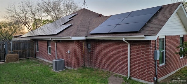 property exterior at dusk featuring central AC unit, a lawn, and solar panels