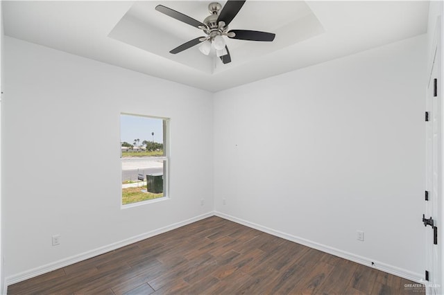 spare room featuring dark hardwood / wood-style floors, ceiling fan, and a tray ceiling