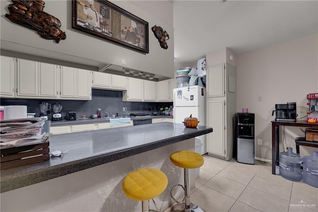 kitchen with a breakfast bar, white cabinets, white fridge, and light tile patterned floors