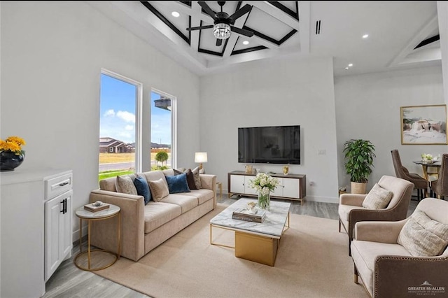 living room featuring coffered ceiling, ceiling fan, a towering ceiling, and light hardwood / wood-style floors