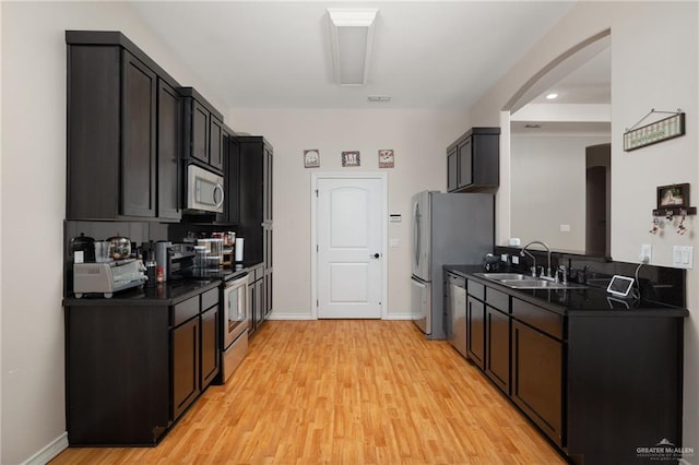 kitchen with dark countertops, appliances with stainless steel finishes, light wood-style floors, and a sink