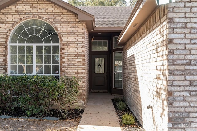 view of exterior entry featuring brick siding and roof with shingles