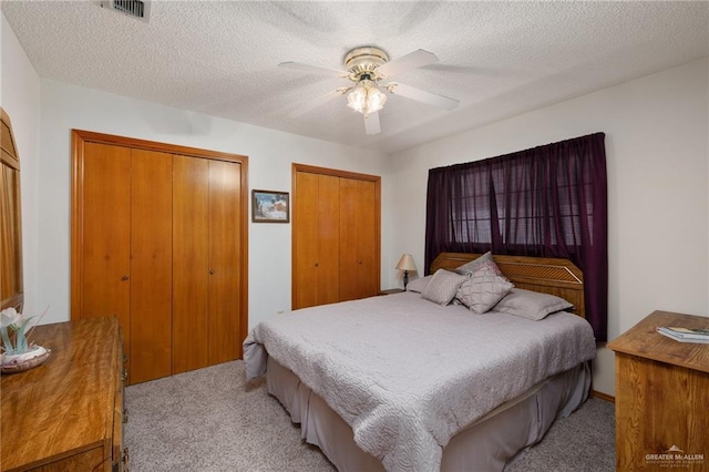 carpeted bedroom with ceiling fan, two closets, and a textured ceiling