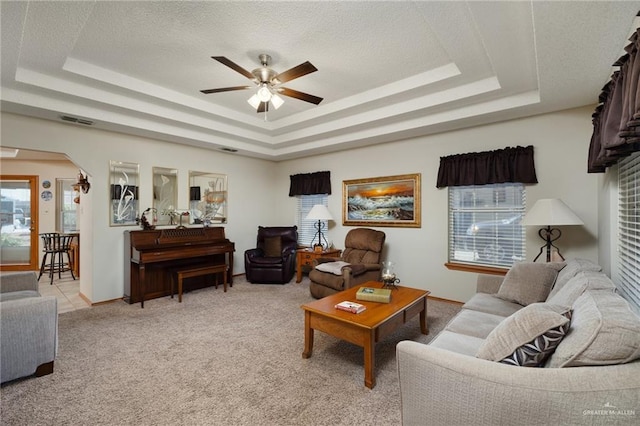 living room featuring a raised ceiling, light colored carpet, a textured ceiling, and ceiling fan