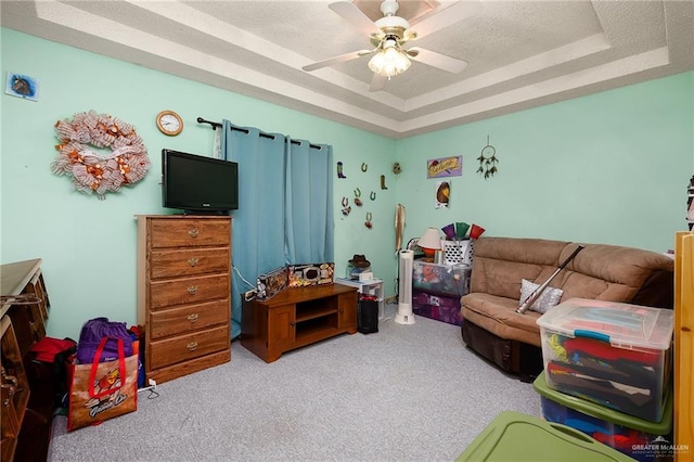 rec room with a raised ceiling, light carpet, ceiling fan, and a textured ceiling