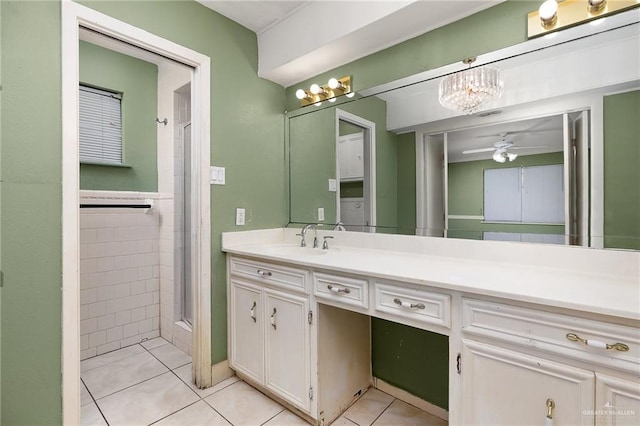 bathroom with ceiling fan with notable chandelier, tile patterned flooring, a shower with door, vanity, and tile walls