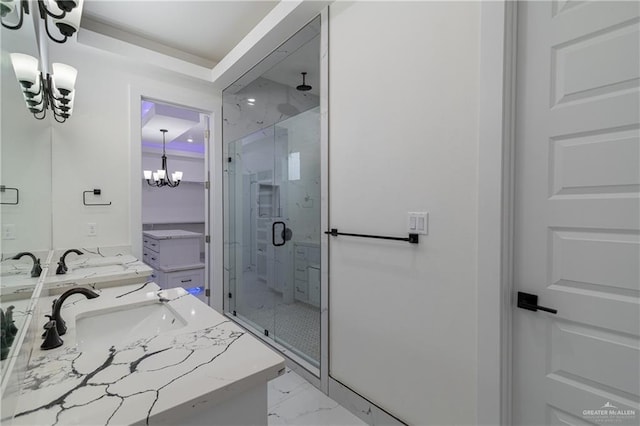 full bath featuring a notable chandelier, a sink, marble finish floor, a shower stall, and double vanity