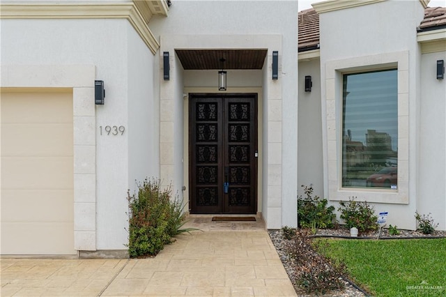 view of exterior entry with an attached garage and stucco siding