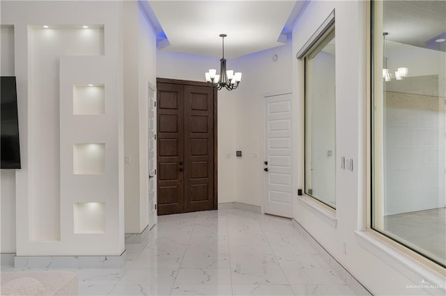 entryway featuring marble finish floor, a notable chandelier, and baseboards