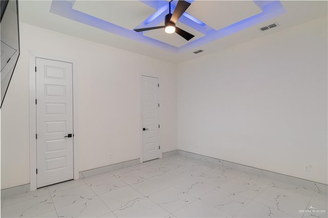 empty room featuring marble finish floor, a raised ceiling, visible vents, a ceiling fan, and baseboards